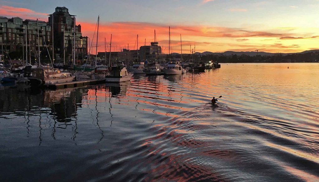 A lone kayaker at sunset paddles by Fisherman's Wharf in Victoria BC.