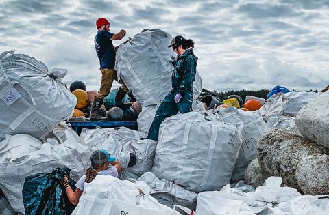 Team members stand on mountains of garbage bags as they sort trash on the barge