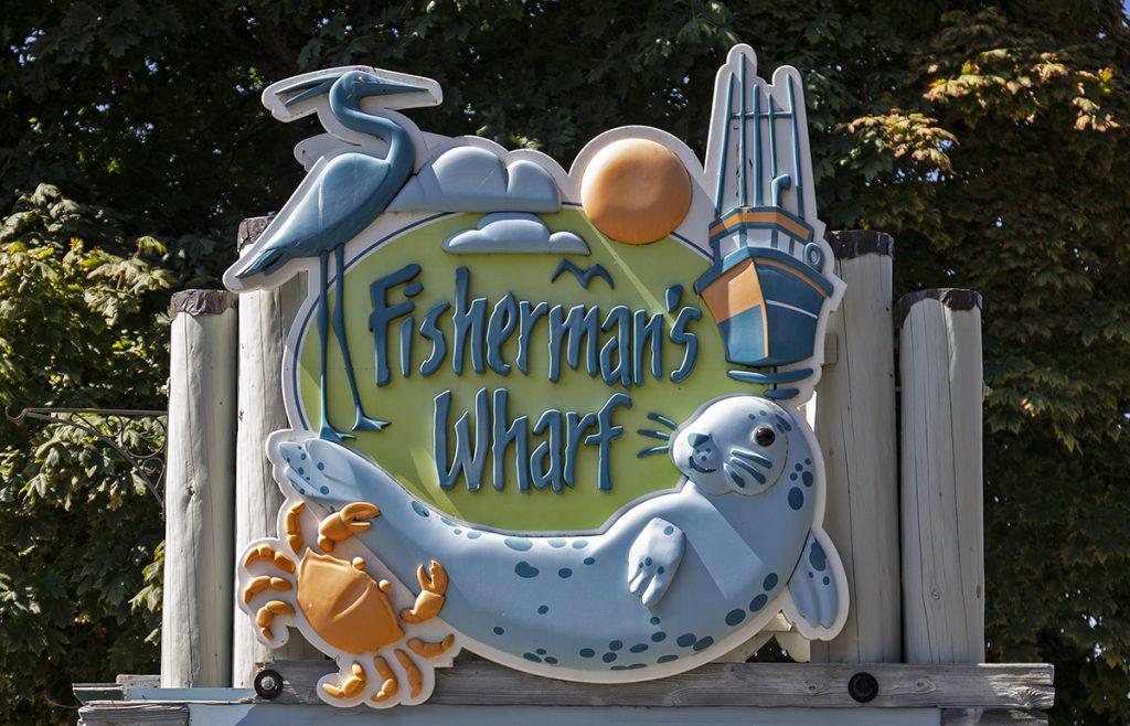 The sign at the entrance to Fisherman's Wharf, showing a fishing boat, a seal, a heron and a crab.