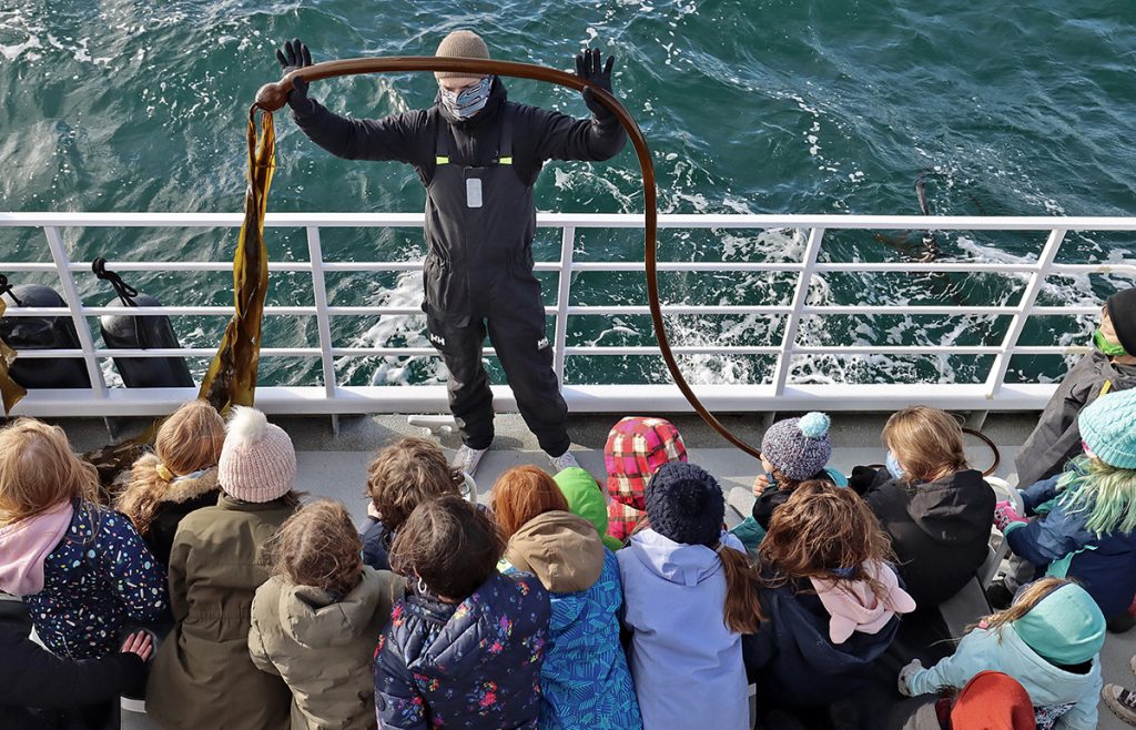 Naturalist Karac holds up a piece of bull kelp in front of young students during a school trip